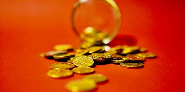A collection of golden coins spilling from a glass jar on a vibrant red background symbolizes wealth.